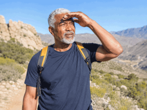 What are cataracts? A senior man struggles with bright sunlight and glare while hiking, a common cataract symptom.