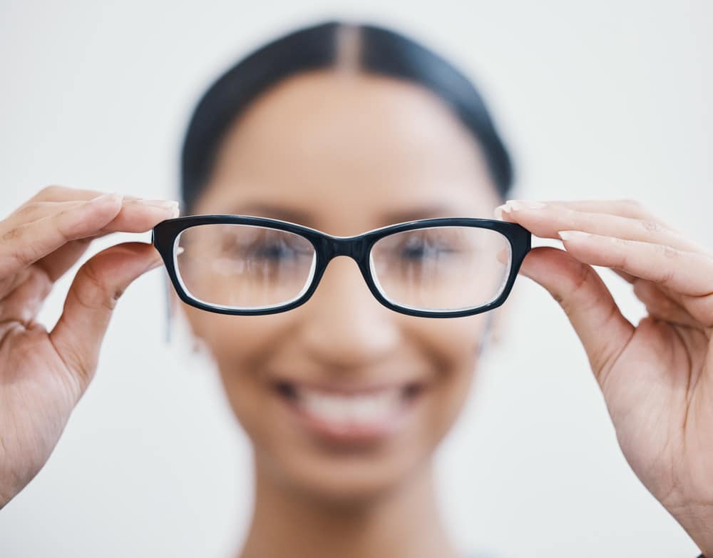 A young woman is thinking about LASIK at her consultation due to blurry vision as she holds up her glasses.