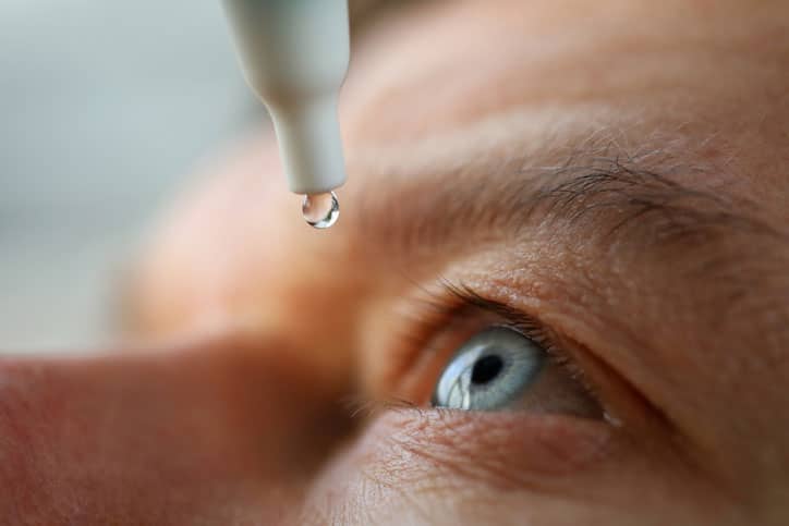 A glaucoma patient is placing eye drops into their eyes.