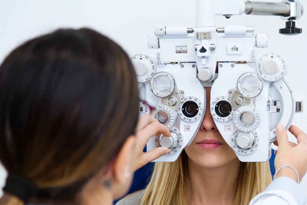 Patient undergoing a vision test with a phoropter as an eye-care professional adjusts the lenses.