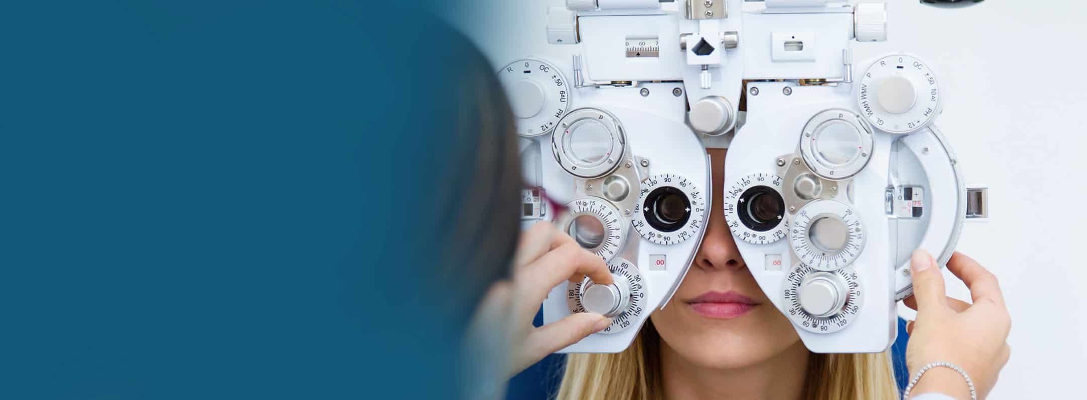 Patient undergoing a vision test with a phoropter as an eye-care professional adjusts the lenses.