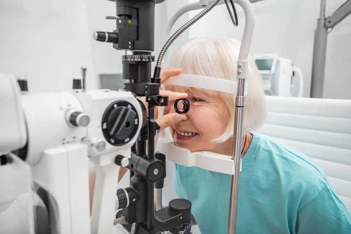 An older woman undergoes SLT (Selective Laser Trabeculoplasty) treatment for glaucoma, sitting at a slit lamp in a bright, modern eye clinic.