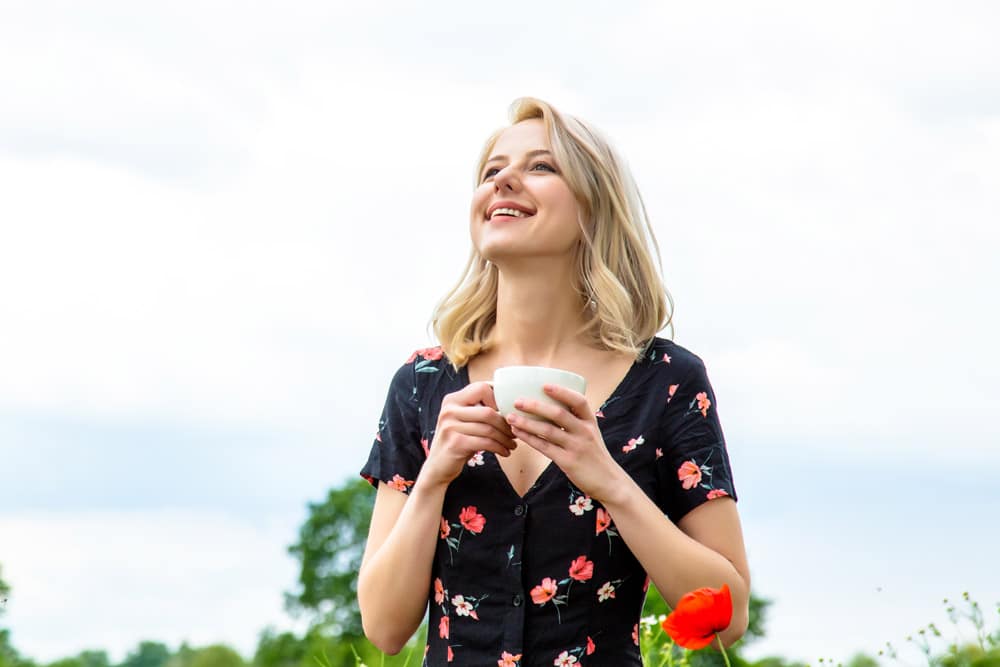 Young woman standing outside enjoying her cup of coffee with clear vision after LASIK.