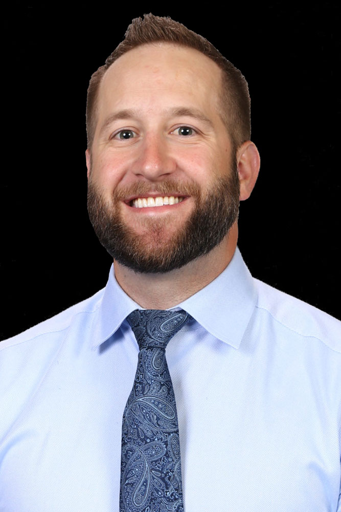 Professional headshot of optometrist Dr. Matthew Hepworth, in a light blue shirt and tie, smiling in front of a black backdrop.