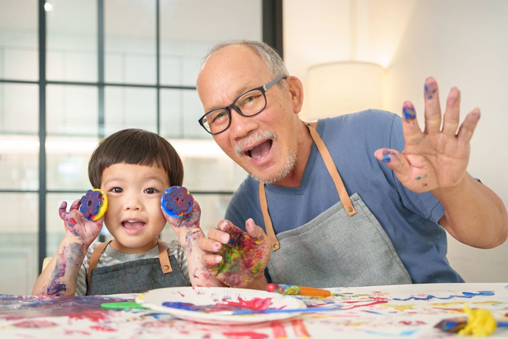Grandfather with glasses and a young child painting together, showing healthy vision and joyful family moments.