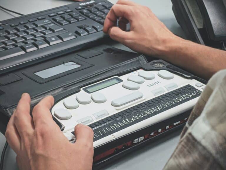 Close-up of a student using a refreshable braille display alongside a computer keyboard, representing College Resources for Visually Impaired Students and tools that support accessible learning and communication.
