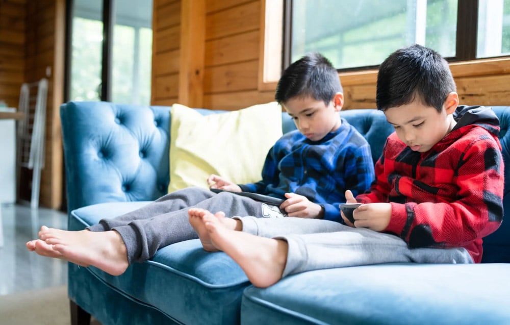 Children sitting on a couch focused on mobile screens.