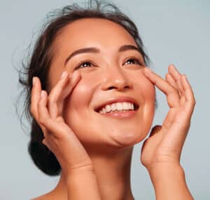 Smiling woman touching under her eyes, representing a positive cataract surgery recovery experience