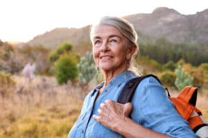 Elevation and retina surgery what’s the connection? Senior woman with backpack looking out over a mountain landscape, illustrating safe return to outdoor activities after surgery