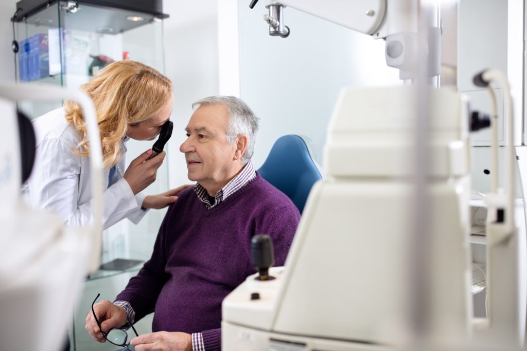 Eye exam room an eye doctor is performing a manual eye exam on a senior male patient who is holding his eye glasses