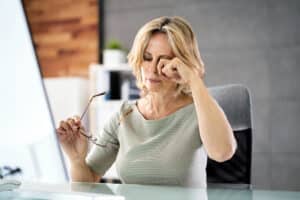 Woman rubbing her eyes from dry eye symptoms at computer