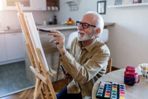 Smiling man painting at easel as part of preparing for your corneal transplant recovery