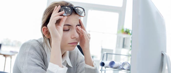 Woman sitting at a desk with a computer, holding her temples and looking stressed.