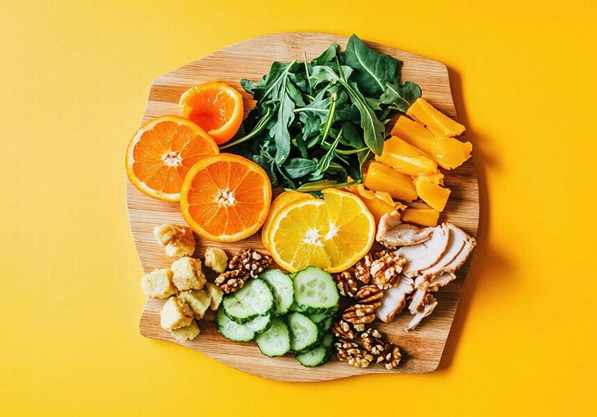 Top 5 Nutrient-Rich Foods for Better Eye Health: Top-down view of a wooden board with sliced oranges, leafy greens, cucumber rounds, walnuts, chicken strips, and cheese—all foods that support eye health