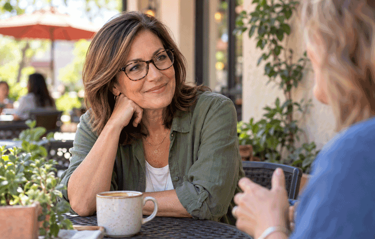 Woman wearing prescription glasses while talking with a friend at an outdoor café.