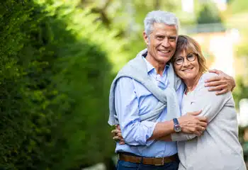 Smiling older couple embracing outdoors before cataract surgery preparation.