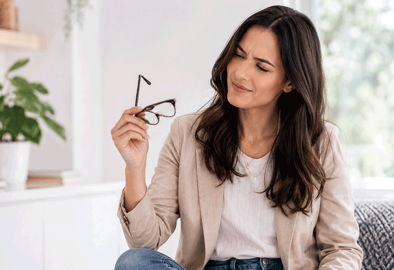 Woman looking confused while holding her glasses, representing nearsightedness treatment options at Barnet Dulaney Perkins Eye Center.