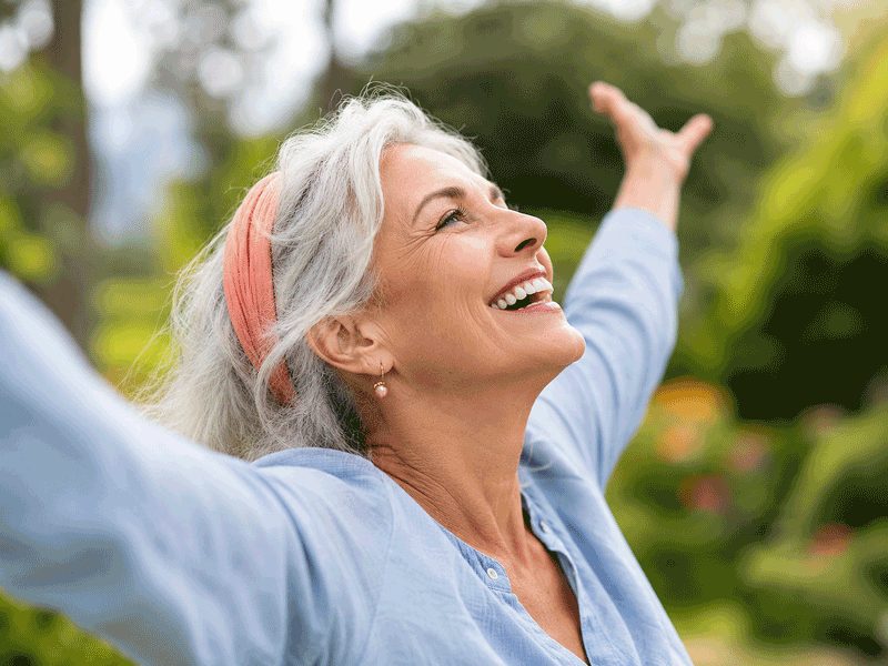 Smiling senior woman raising her arms outdoors for the Barnet Dulaney Perkins Eye Center what are cataracts blog