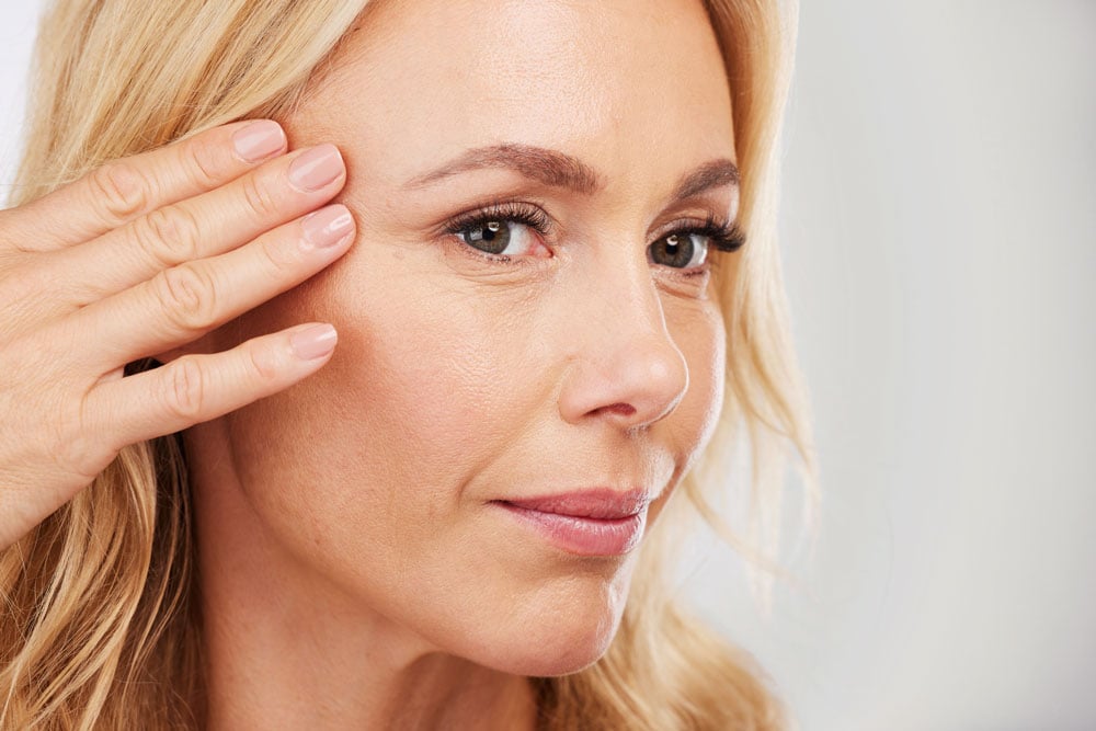 Woman touching the skin beside her eye while considering eyelid surgery.