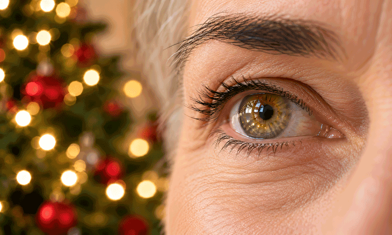 Close-up eye reflecting Christmas lights beside a blurred tree, for Barnet Dulaney Perkins Eye Center’s Christmas tree cataract article.