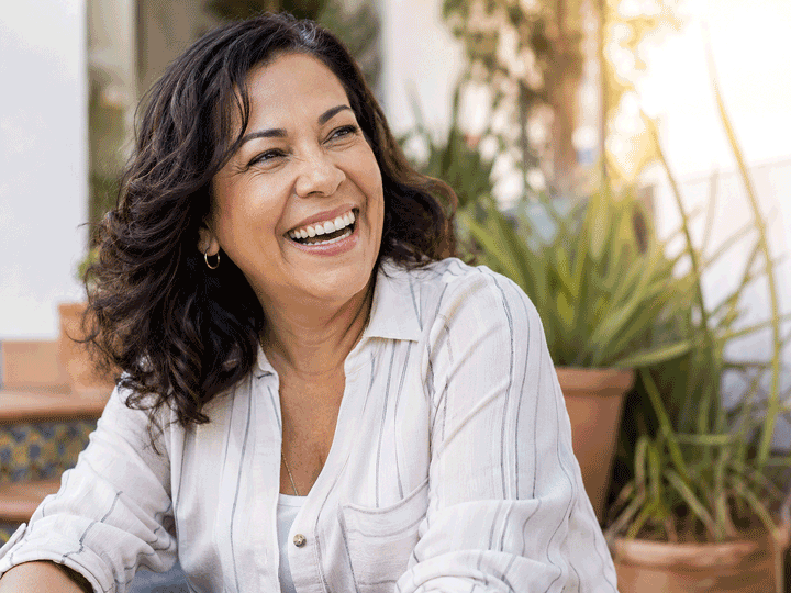 50-year-old woman laughing outdoors while looking off camera, illustrating life moments worth protecting through panuveitis symptoms and treatment at Barnet Dulaney Perkins Eye Center.
