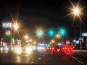 Nighttime street view with bright headlight halos, glare, and glowing signs, illustrating light sensitivity and possible red eye causes for Barnet Dulaney Perkins Eye Center.