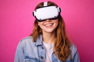 happy teen girl smiling while using wearable tech devices with a VR headset in front of a bright pink background at Barnet Dulaney Perkins Eye Center